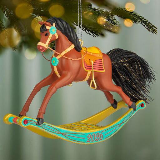 Decorative rocking horse ornament with a saddle, bridle, and '2026' on a green blurred background.