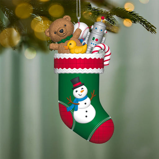 Christmas stocking ornament with teddy bear, robot, and candy on a blurred green background