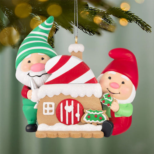 Christmas ornament with two elves and a gingerbread house, hanging from a tree.