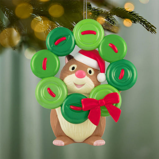 Christmas ornament of a hamster with a wreath made of buttons and red bow, hanging on a tree.