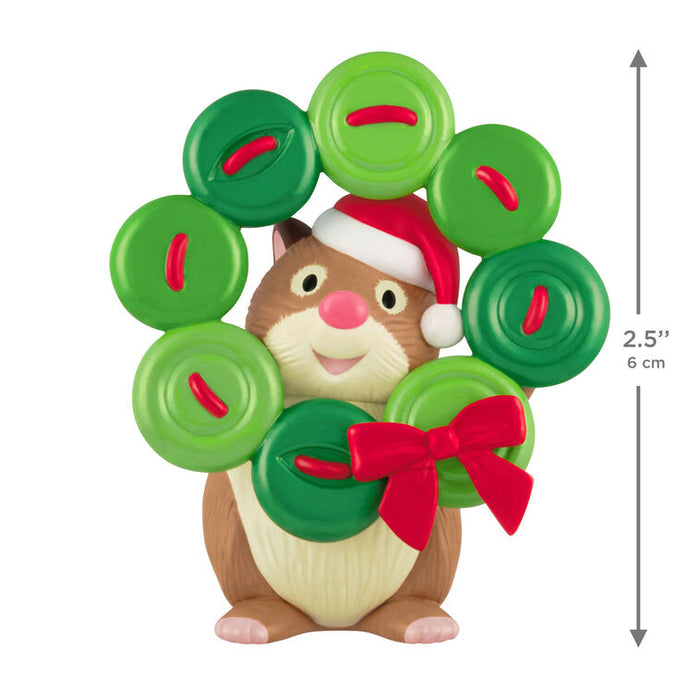 Hamster figurine wearing a Santa hat with a green wreath made of buttons and red bow, on a white background.