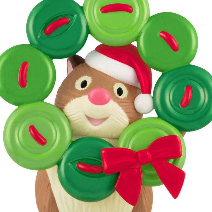 Hamster figurine wearing a Santa hat surrounded by green and red circular decorations on a white background