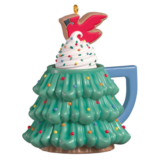Decorative Christmas ornament shaped like a mug with a swirl of whipped cream and sparkles and topped with a cardinal cookie on top, on a white background.