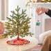 Small decorated Christmas tree on a table with a person holding an ornament.