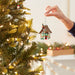 Hand placing a Christmas ornament on a tree with blurred festive background