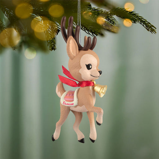 Deer ornament with a red scarf and bell hanging on a Christmas tree.