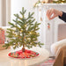 Small decorated Christmas tree on a table with a person's hand placing a ornament.
