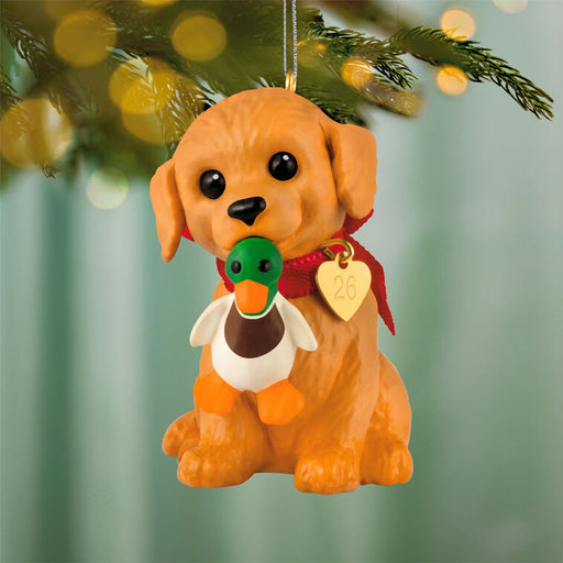 Dog-shaped Christmas ornament with a duck toy in its mouth, hanging on a tree.