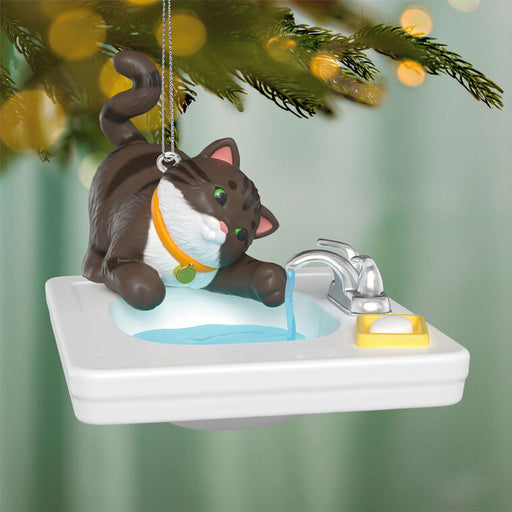 Cat ornament on a sink with water flowing, hanging from a Christmas tree.