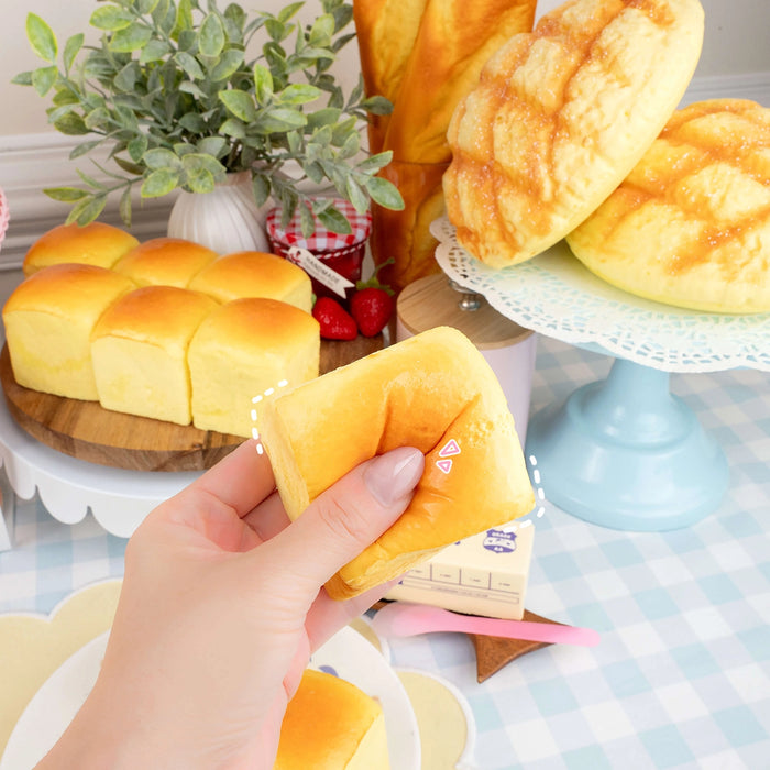 Hand holding a small loaf of bread with more bread and plants in the background.