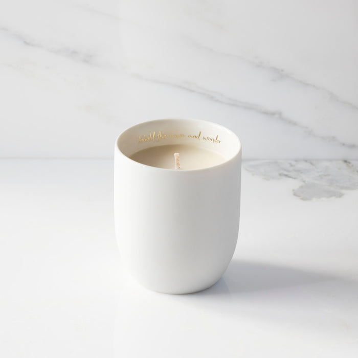 White candle in a ceramic holder on a marble surface