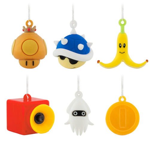 Six Nintendo-themed plush character ornaments hanging from white strings on a plain white background, including an orange mushroom, blue shell, banana peel, red camera, white squid, and gold coin.