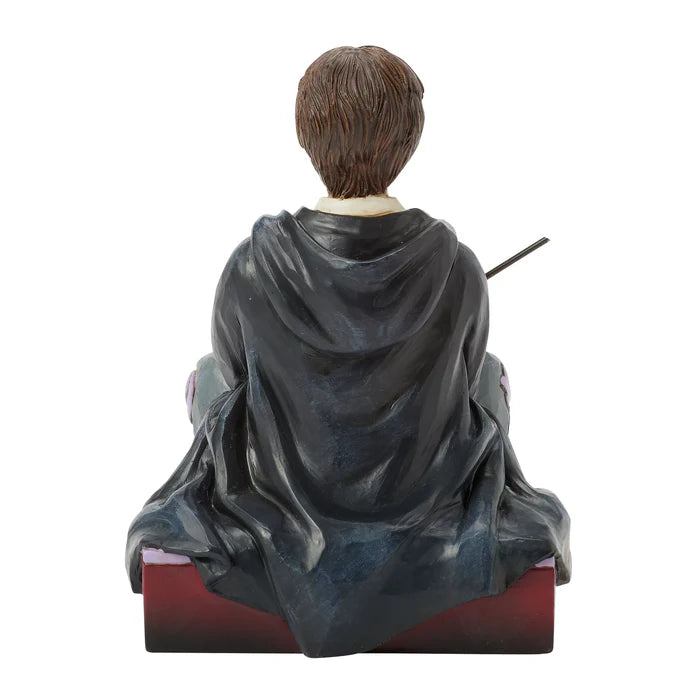 Statue of a person in a dark robe with a wand, sitting on a red platform, on a white background