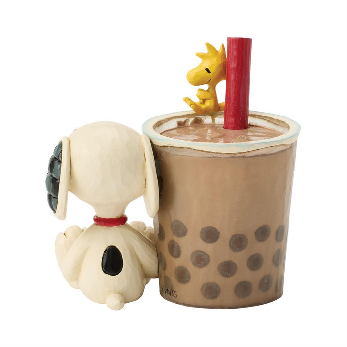 Snoopy figurine next to a bubble tea with a dragon toy on top, on a white background