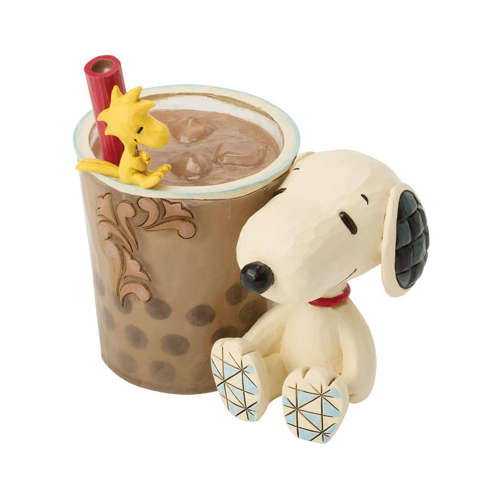 Snoopy figurine next to a cup of hot chocolate with a straw and yellow character on a white background
