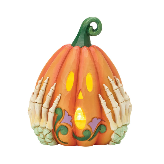 Decorative pumpkin with skeleton hands and a lit candle inside on a white background
