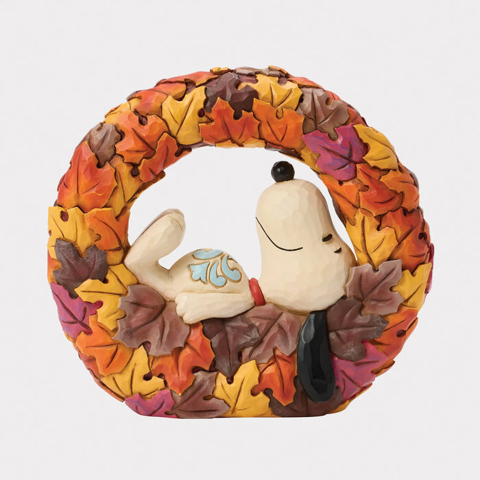 Snoopy figurine inside a wreath made of autumn leaves on a white background