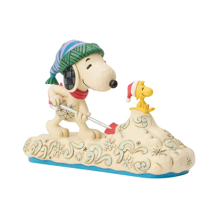 Decorative figurine of Snoopy and Woodstock shoveling snow with festive hats on a white background