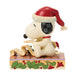 Snoopy figurine wearing a Santa hat on a decorative base with holly leaves and berries.