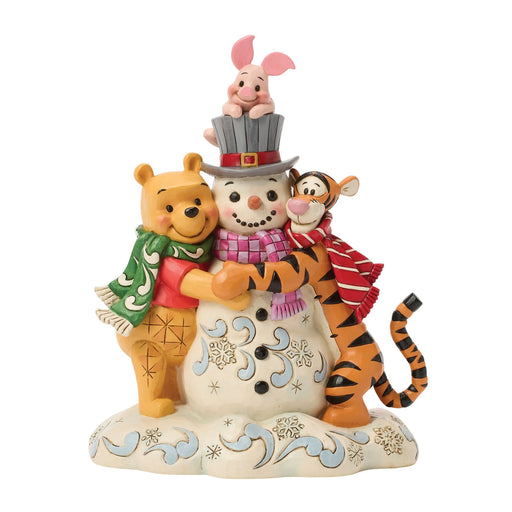 A Disney Winnie the Pooh and his friends winter holiday figurine featuring Winnie the Pooh hugging a snowman, Tigger on one side, and Piglet sitting on top of the snowman's hat, all set against a plain white background.