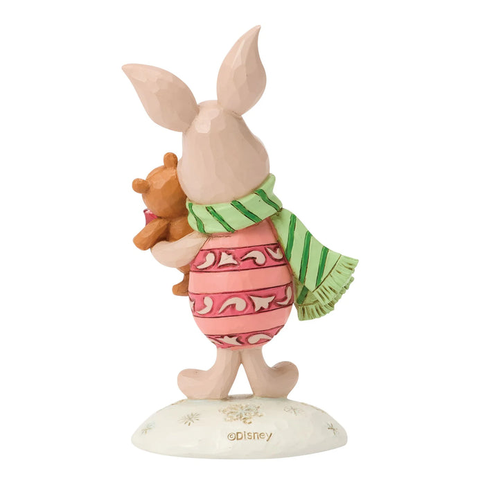 Figurine of a piglet character holding a bear, wearing a pink dress with a green scarf, on a white background.