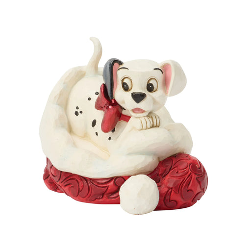 Dog figurine with a red bow sitting on a red cushion against a white background