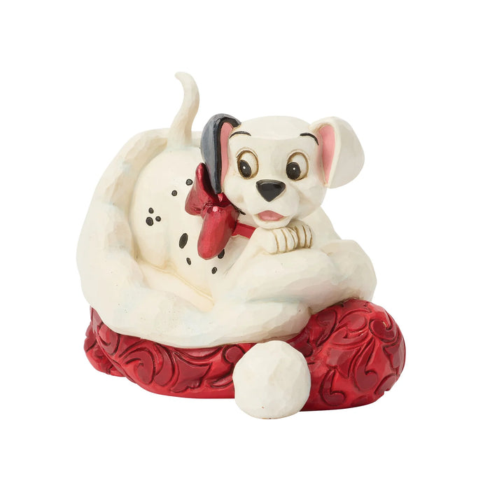 Dog figurine with a red bow sitting on a red cushion against a white background