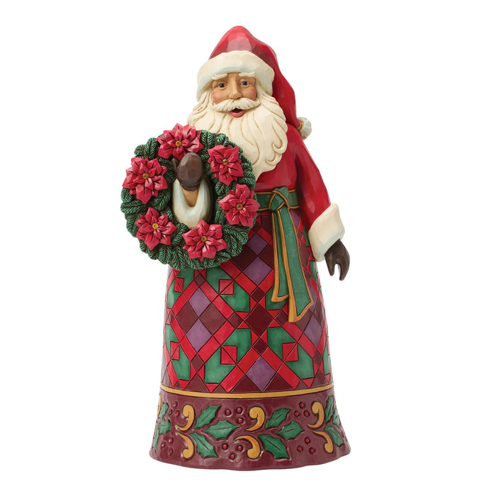 Festive Santa figurine holding a wreath with poinsettias on a white background