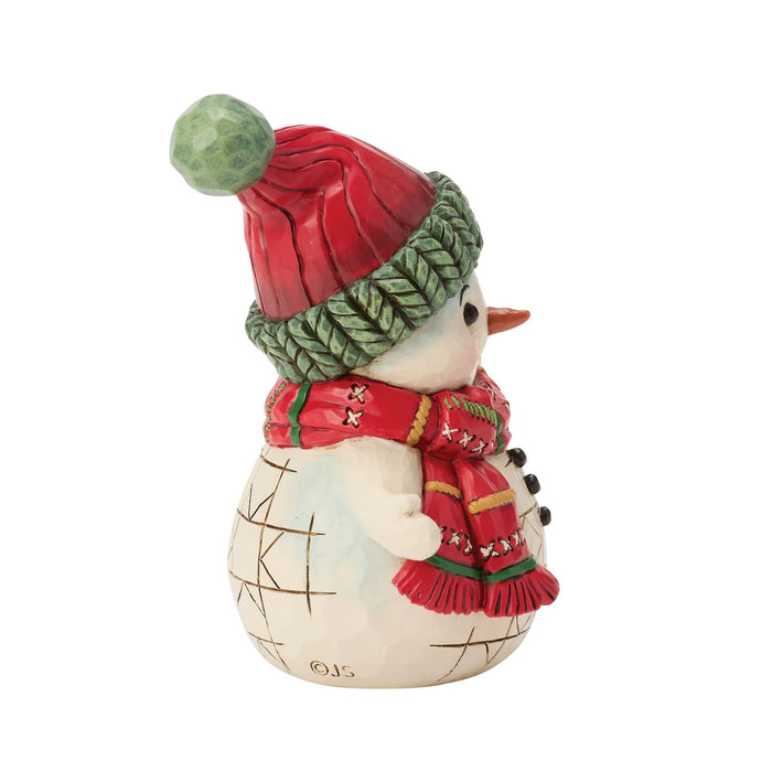 Snowman figurine with red and green hat and scarf holding a bell on a white background