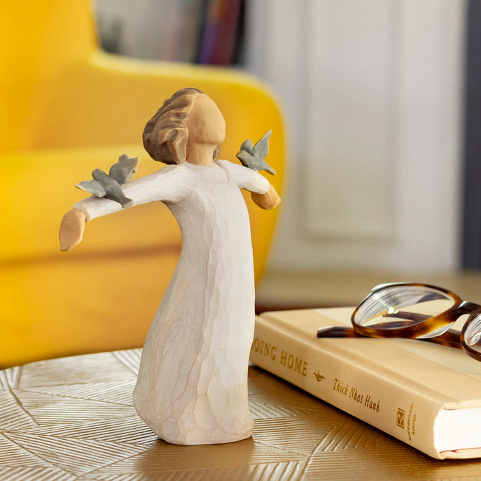 Decorative figurine of a woman with doves on a table with books and glasses.