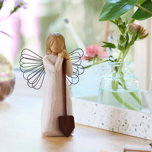 Decorative angel figurine with a shovel in a home setting with flowers and decor.
