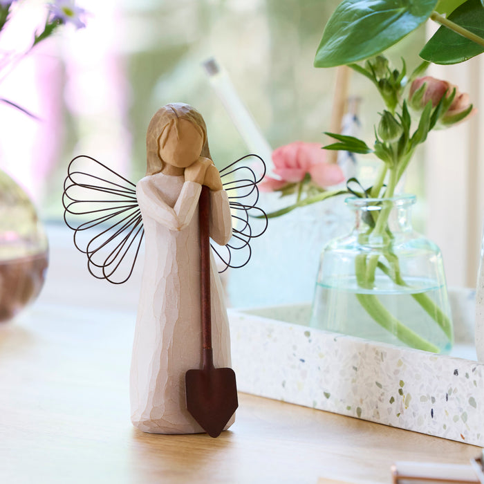 Decorative angel figurine with a shovel in a home setting with flowers and decor.
