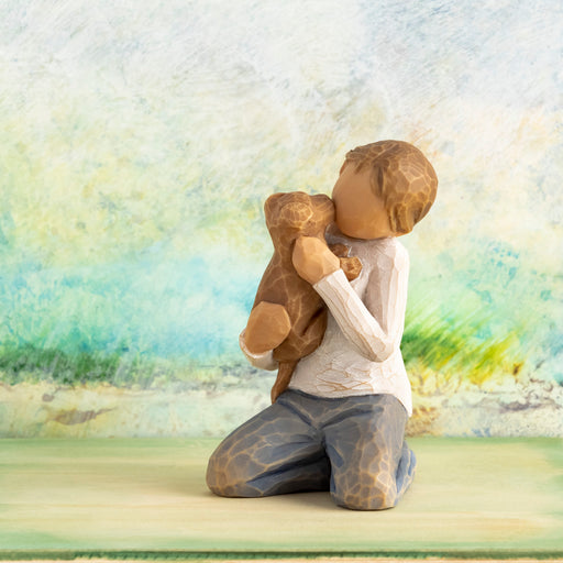 Wooden figurine of a person hugging a teddy bear with a scenic background