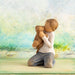 Wooden figurine of a person hugging a teddy bear with a scenic background