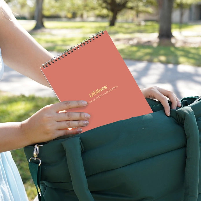 Person holding a pink notebook with 'Lifelines' branding outdoors.