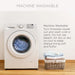 White washing machine with clothes inside, next to a basket of folded clothes on a wooden floor.