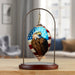 A decorative hanging ornament shaped like a teardrop, featuring a painted bald eagle over an American flag design, suspended from a metal stand with a wooden base on a tabletop. The background shows a softly blurred living room interior.