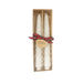 Two white candles in a cardboard box with a plaid ribbon and tag on a white background