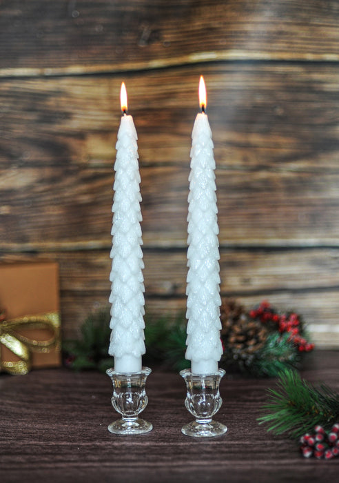 Two white cone-shaped candles in glass holders on a wooden surface with a rustic background.