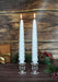 Two white cone-shaped candles in glass holders on a wooden surface with a rustic background.