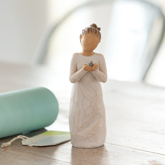 Decorative figurine of a woman holding a bird on a wooden surface with a blurred background