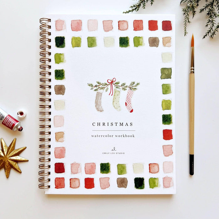 Christmas watercolor workbook with color swatches and a pen on a white surface.