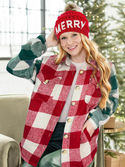 Person wearing a red and green plaid jacket with a 'MERRY' beanie in front of a Christmas tree.