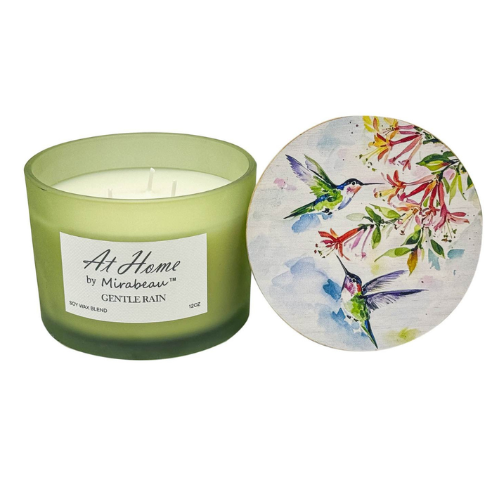 Green candle with a decorative lid featuring hummingbirds and flowers on a white background