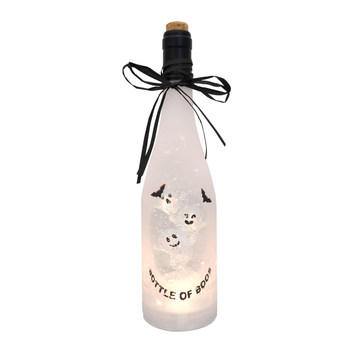 A frosted glass bottle with a cork stopper, decorated with a black ribbon bow and featuring printed ghost illustrations and the text 'BOTTLE OF BOO'. The bottle is illuminated from within with warm white fairy lights, set against a plain white background.