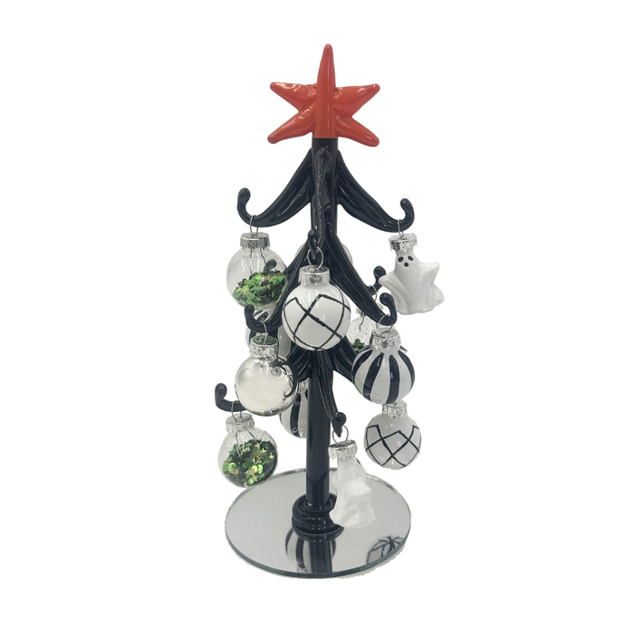 A black decorative tabletop Christmas tree with a red star topper and hanging ornaments, including clear baubles with black patterns, white ghosts, and green glitter, on a plain white background.