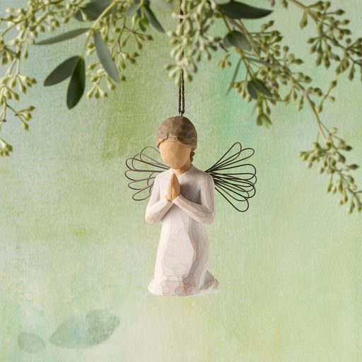 Angel figurine with butterfly wings hanging against a light green background with foliage.