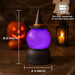 A purple glowing crystal ball Halloween decoration on a black base with a witch hat, shown on a wooden surface with dimension lines indicating 8.5 inch height and 4.