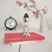 Decorative angel figurine on a pink book with a clock and flowers in the background