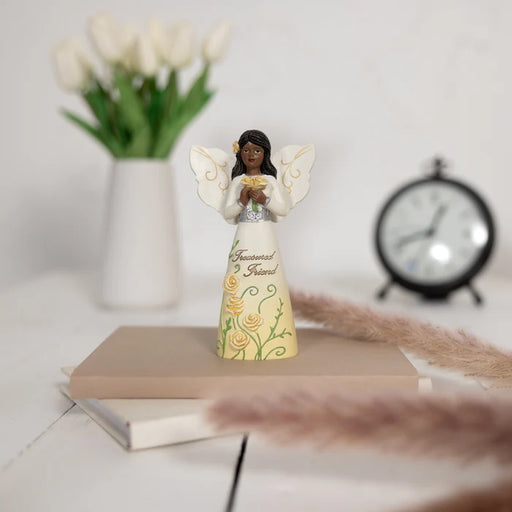 Decorative angel figurine with flowers on a surface with a clock and vase in the background.
